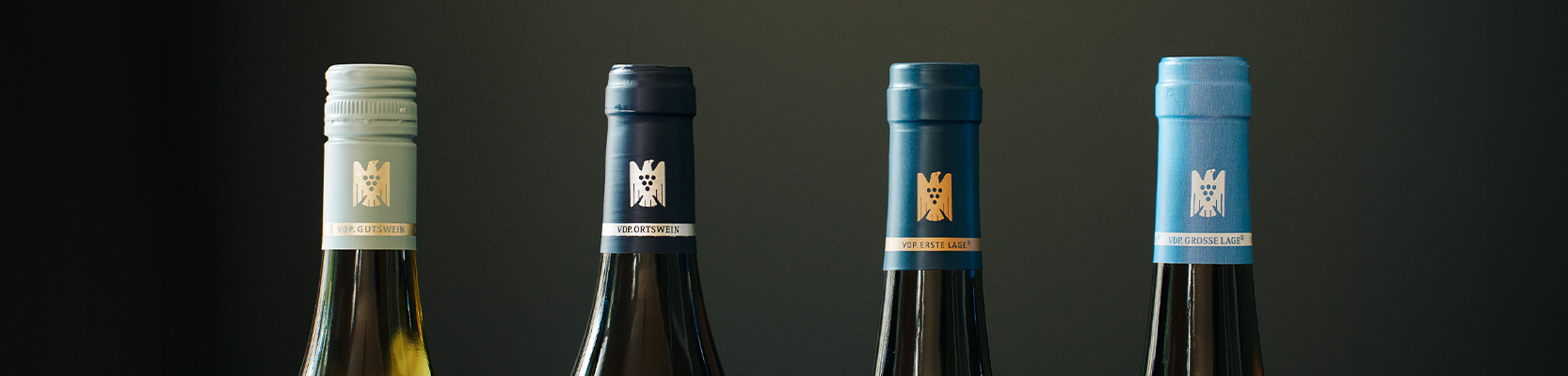 Verschiedene VDP Weinflaschen nebeneinander vor dunklem Hintergrund.