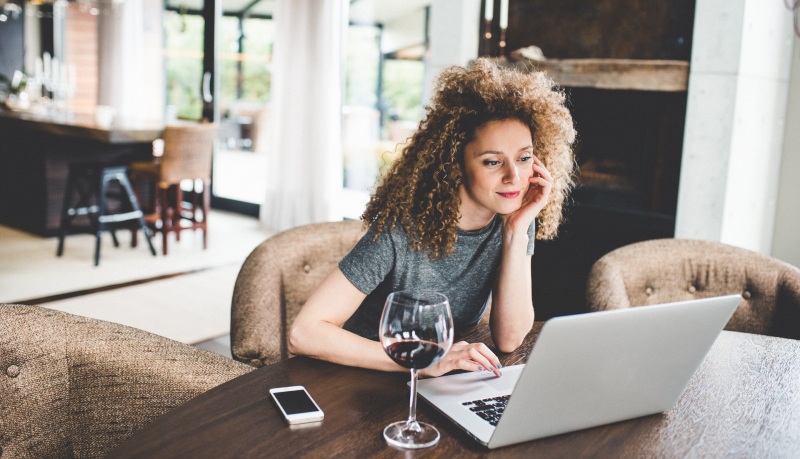 Frau trinkt Wein und recherchiert am Laptop