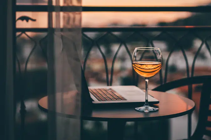 Laptop neben Weinglas im Sonneruntergang auf dem Balkon