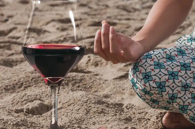 Rotweinglas neben meditierender Frau am Strand